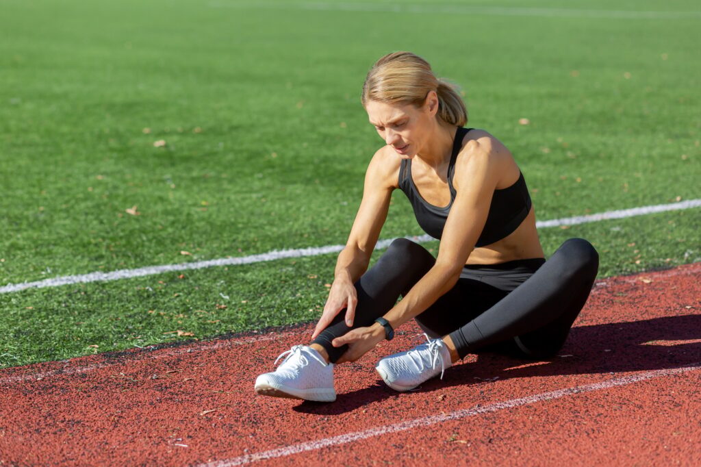Female athlete experiencing a painful ankle injury while training on a running track